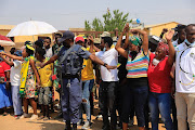 A police officer tries to control a group of protesting community members outside the home of slain ANC councillor Tshepo Motaung on Tuesday. A high-level delegation visited the family after Motaung was brutally killed on Friday.