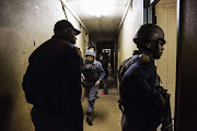 South Africa policemen proceed with a search for drugs and weapons during a South African Police and South African army raid at Madoda Hostel in the Alexandra township of Johannesburg on April 23, 2015. South African soldiers deployed last night to tackle gangs hunting down and killing foreigners after at least seven people died in a wave of anti-immigrant violence.   AFP PHOTO / GIANLUIGI GUERCIA