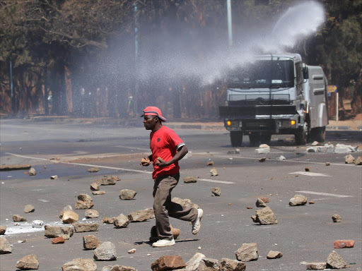 A man runs from a water cannon as opposition party supporters clash with police in Harare, Zimbabwe, August 26, 2016 /REUTERS