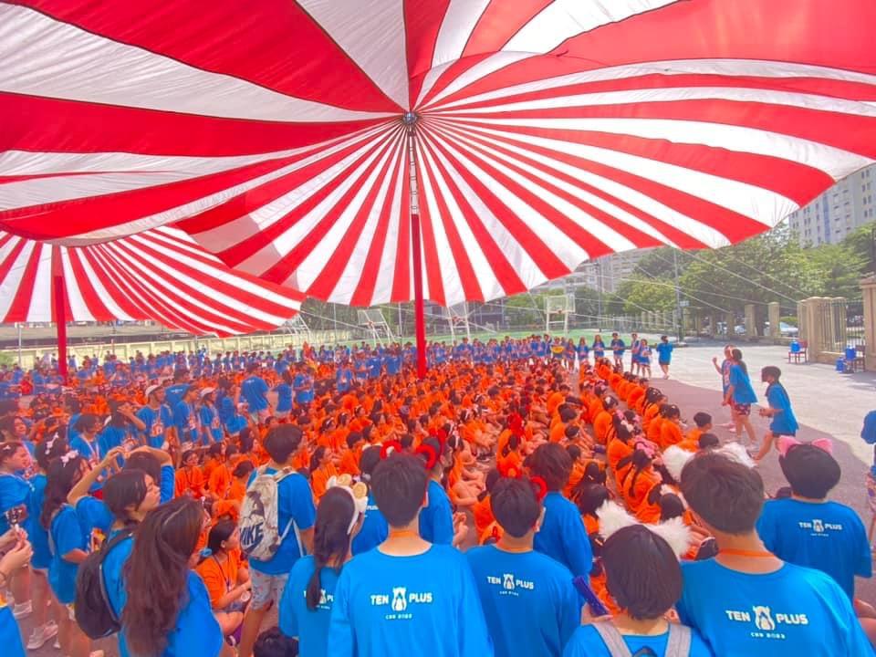 A large group of people under a large striped tent</p>
<p>Description automatically generated