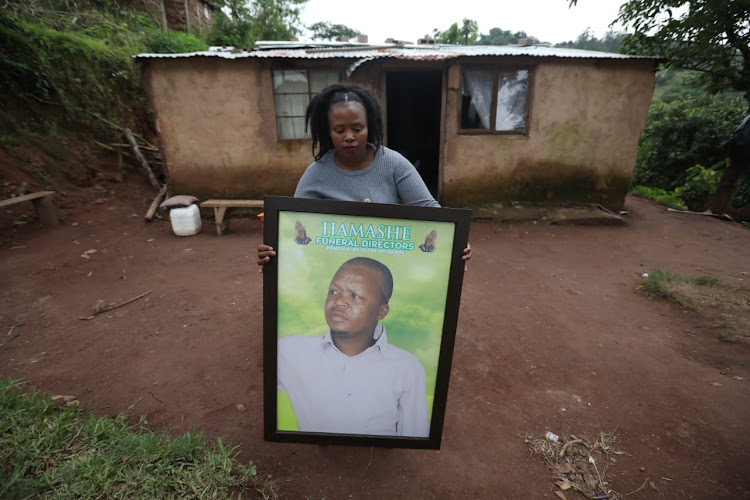 Thandaza Mtshali holds a framed photograph of her late uncle Sifiso Mtshali who was buried on Sunday. Mtshali was not married and had 38 children, whose names and contact details he recorded in a black notebook.