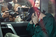 An unidentified man hides his face as members of the media photograph a car departing the offices of Serbian tennis player Novak Djokovic's legal team under police escort on January 15, 2022 in Melbourne, Australia. Djokovic is in detention and faces deportation after his visa was cancelled by the Australian government. A hearing to hear his appeal is scheduled for Sunday, one day before Djokovic is scheduled to play in the Australian Open.