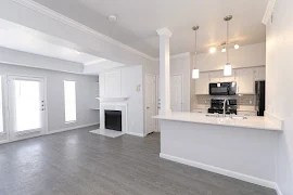 Open concept living room with wood-inspired flooring, fireplace, barstool countertop area with modern hanging light fixtures and view of the kitchen