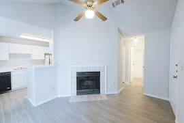 Living room with wood-inspired flooring, fireplace with tile surrounding it, ceiling fan, grey walls, and light trim