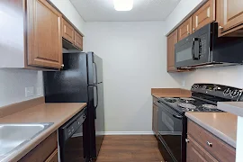 Kitchen with dark wood cabinets, brown countertops, dark wood floors, black appliances, dome light, white walls, white trim