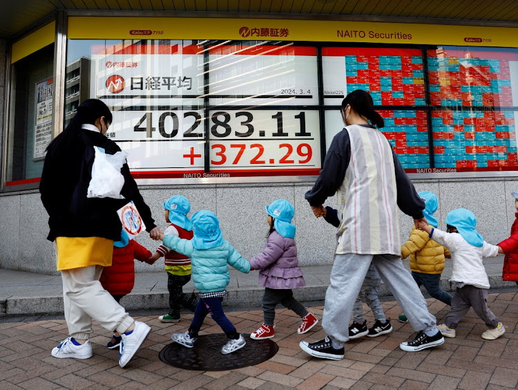 Children and their teachers walk past an electronic screen displaying Japan’s Nikkei share average outside a brokerage in Tokyo, Japan, on March 4 2024. Picture: REUTERS/KIM KYUNG-HOON