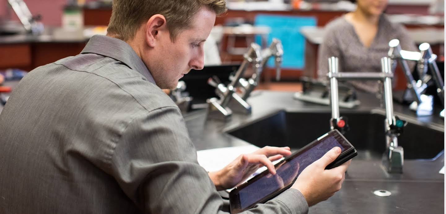 Jeune enseignant regardant une tablette dans une salle de laboratoire de sciences physiques.