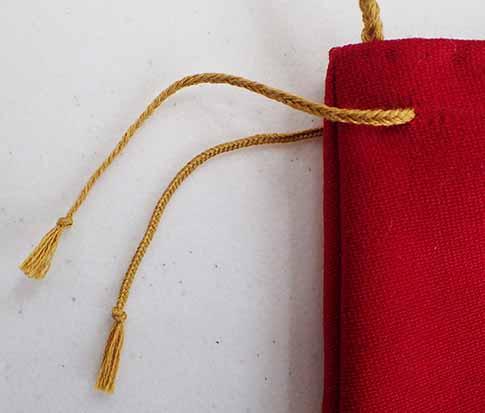 The two gold drawstring threads, knots and excess thread visible to the left hand side, pulled through the final holes on each side of the red bag. 