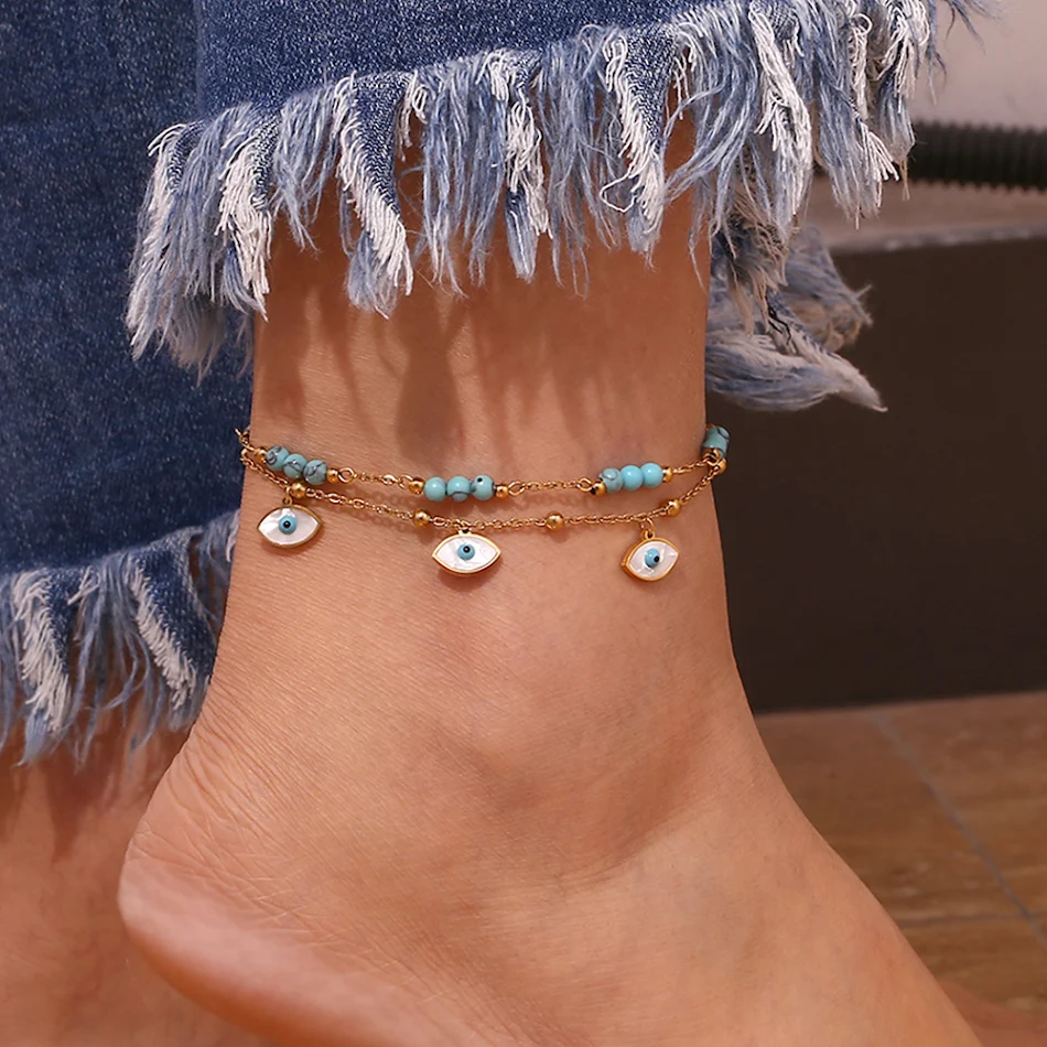 Witte schelp enkelbandje met turkoois ogen en dubbele cirkel, een stijlvolle toevoeging aan je zomeroutfit.