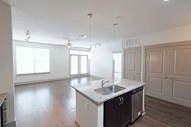 View from the kitchen island with a stainless steel sink and dishwasher facing the living room with a large window