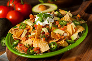 Homemade Unhealthy Nachos with Cheese, Sour Cream, and Vegetables.