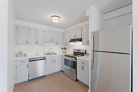 Modern apartment kitchen with white cabinetry, stainless steel appliances, and wooden flooring.