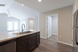 Kitchen with dark cabinets, farmhouse sink, dark wood floors, looking into living room with vaulted ceilings, ceiling fan