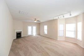 Living room features beige carpet, light walls, white trim, and a corner fireplace ahead next to a set of patio doors