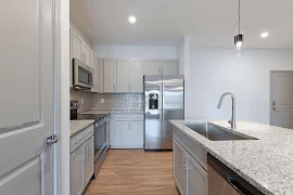 Modern apartment kitchen with stainless steel appliances, white cabinets, and granite countertops.