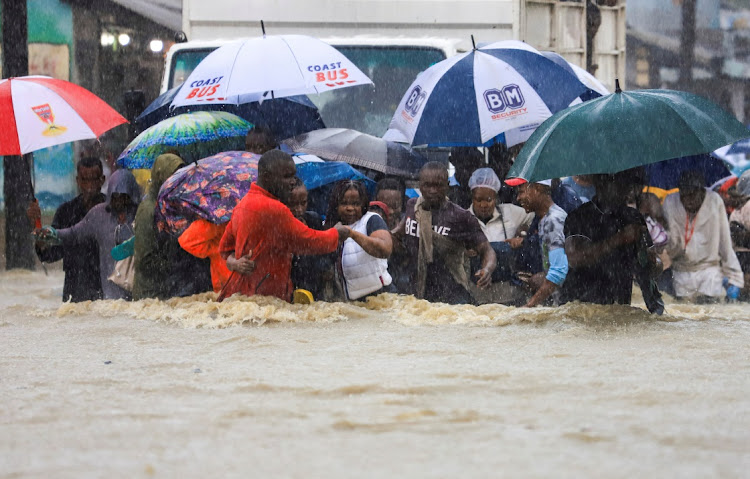 People wade through flood waters along a street following heavy rains in the Kisauni district of Mombasa, Kenya, on November 17 2023.