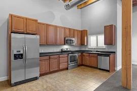 Modern kitchen with stainless steel appliances, wooden cabinets, and tile flooring in an apartment.