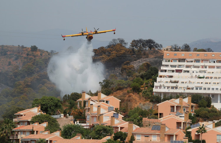 A firefighting plane makes a water drop over buildings near a wildfire burning on Sierra Bermeja mountain, in Estepona, Spain, September 10, 2021.