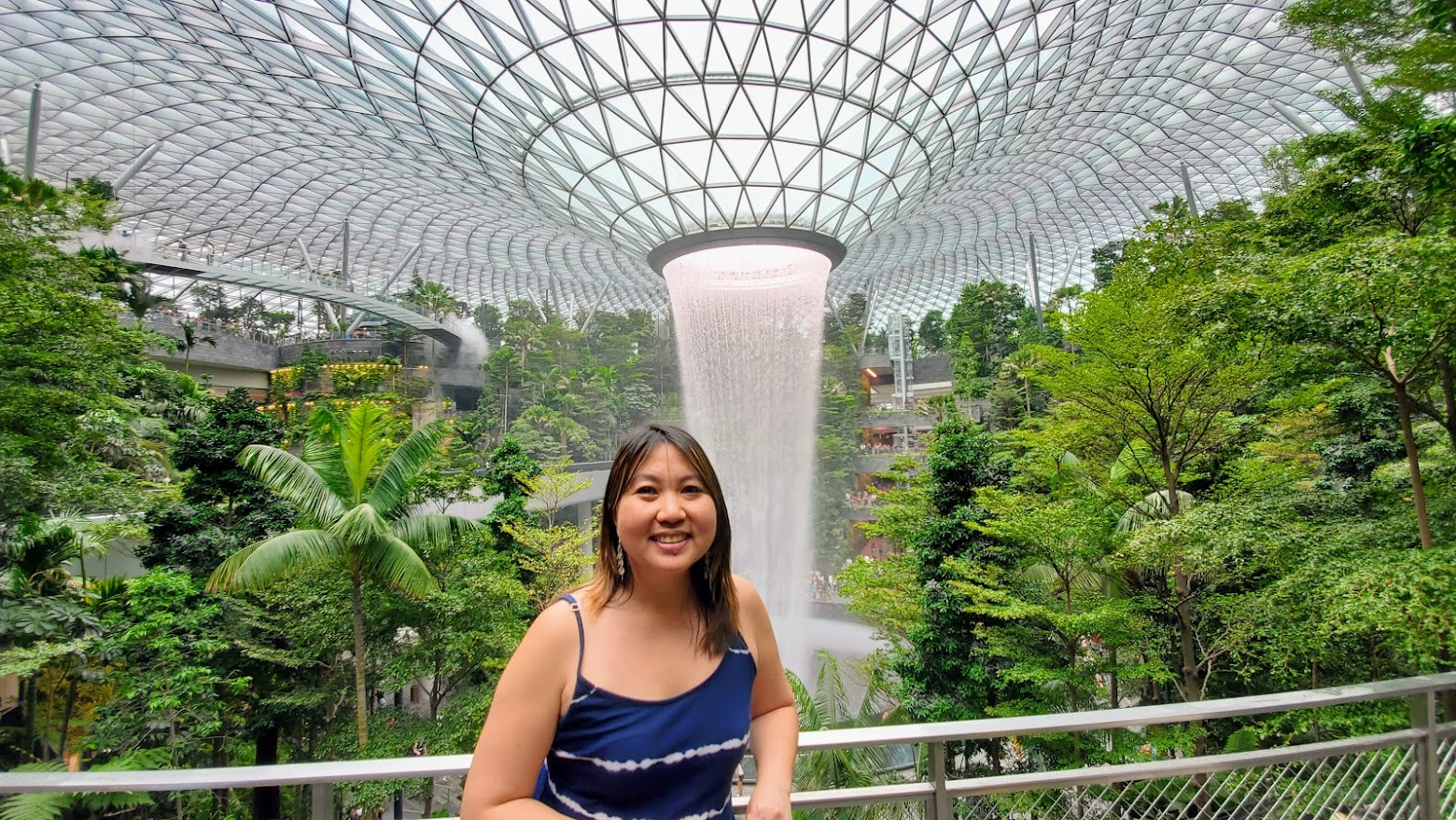 Visiting Changi Airport in Singapore: the famous HSBC Rain Vortex and the surrounding Shiseido Forest Valley - four stories of greenery surrounding the world's tallest indoor waterfall. You can see the Canopy Bridge with its glass floor behind me to my right (left side of photo)