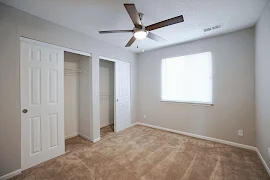 Bedroom with neutral walls & carpet with light trim with a ceiling fan & window with blinds & two closets with sliding doors.