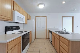 Kitchen with light wood cabinets, white appliances, cream countertops, tan tile floor, sink in peninsula, dome light