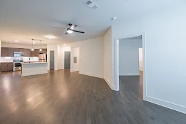 Open concept living room with wood-inspired flooring, light walls and trim, ceiling fan, and access to the kitchen area