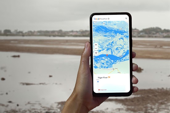 Une main tient un smartphone et l'écran du logiciel de prévision des inondations est visible sur l'écran. Un paysage inondé est représenté en arrière-plan.