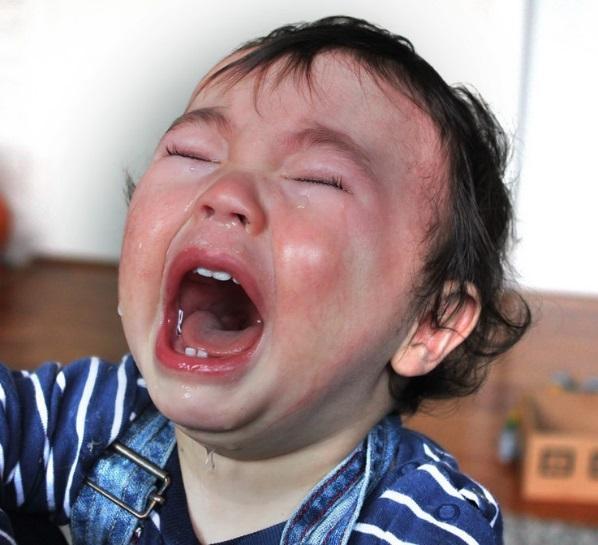 A red-faced toddler screams and cries with tears streaming down her face.