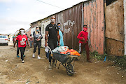 Siya Kolisi and his wife, Rachel, use a wheelbarrow to deliver food in an  East London township as part of their foundation's efforts to ease the plight of the poor. 