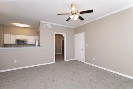 Front door off carpeted living area with ceiling fan adjacent to kitchen with white cabinets and stainless steel appliances