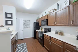 Model unit kitchen with dark wood cabinets, black appliances, dark wood inspired floors, and light colored walls