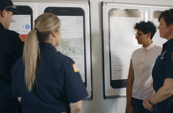 A Googler and three first responders stand in front of posters displaying examples of how a wildfire boundary map appears on Google Search