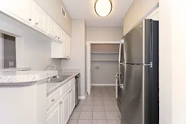 Kitchen with white cabinets and stainless steel appliances, tile flooring and laundry closet with built-in shelves