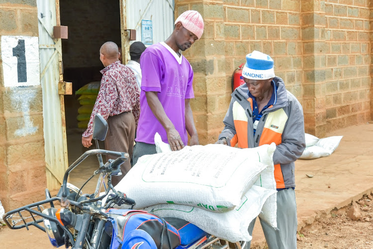 Farmers load bags of fertiliser on a motorbike in their ward collection centre.