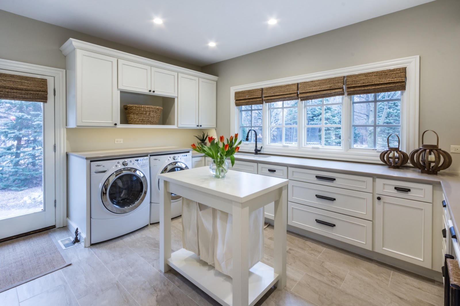 Main floor laundry with ample storage and counter space. Featuring white cabinetry and tile flooring with lots of natural light filtering through the windows and side door.