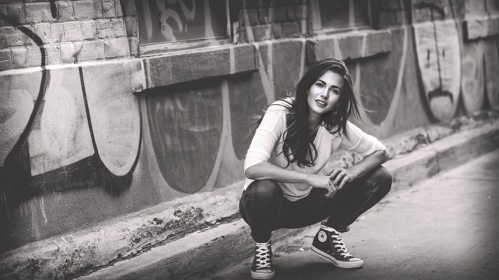 black and white image of young woman crouching down in from of graffiti 