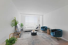 Modern apartment living room with a white sectional sofa, blue armchairs, a central coffee table, and decorative plants.