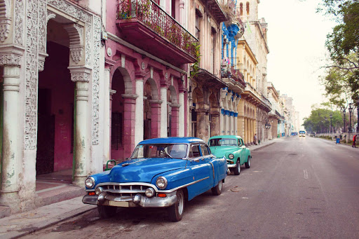 Cuba-Two-Cars-Parked-on-Street-With-Colorful-Buildings2.jpg - Visit Old Havana on a cruise.