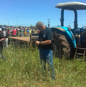 People gathering at the scene where a farm worker was allegedly killed for driving the tractor outside of work.