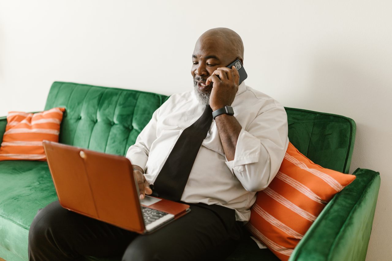 Homem negro mexendo no computador e conversando no telefone celular