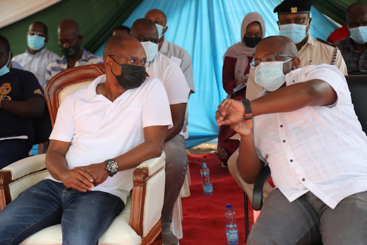 Kilifi Governor Amason Kingi has a word with Housing and Urban Development Principal secretary Charles Hinga during the tittle deed issuance ceremony for informal settlement schemes under KISIP in Malindi