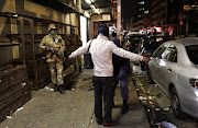 Members of the South African military look on as a police officer searches a man during a patrol as a night-time curfew is enforced in Johannesburg in July 2020.