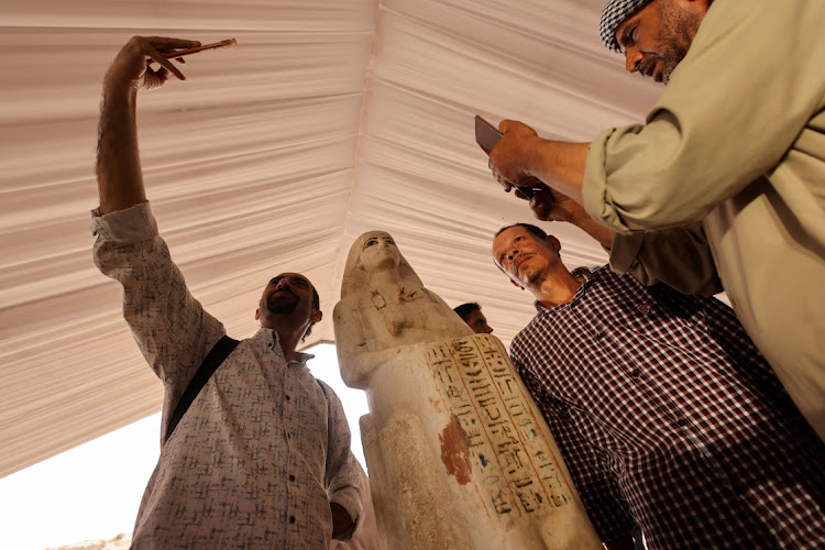 People take pictures with an ancient statue that was recently unearthed at the newly discovered site where two embalming workshops for humans and animals along with two tombs and a collection of artefacts were found, near Egypt's Saqqara necropolis, in Giza, Egypt May 27, 2023.