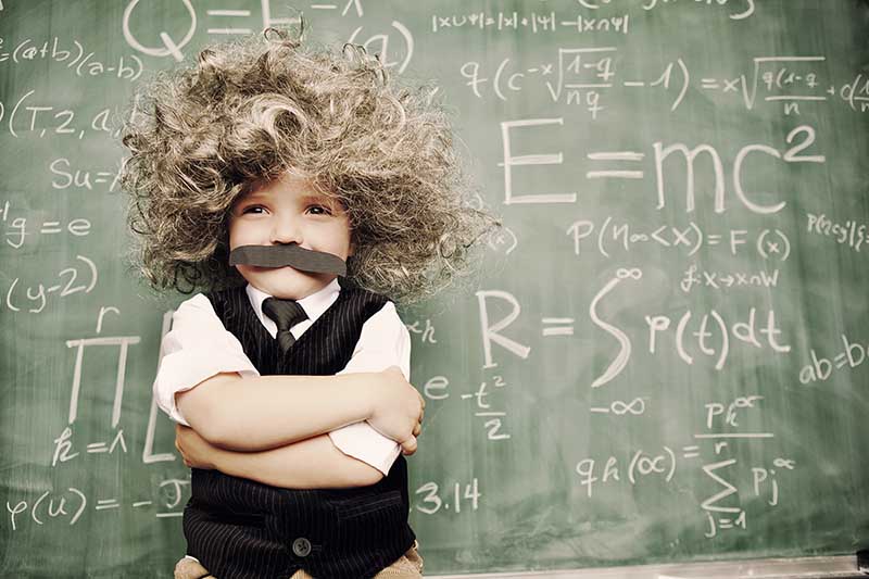 Enfant rigolo déguisé en Einstein devant un tableau noir
