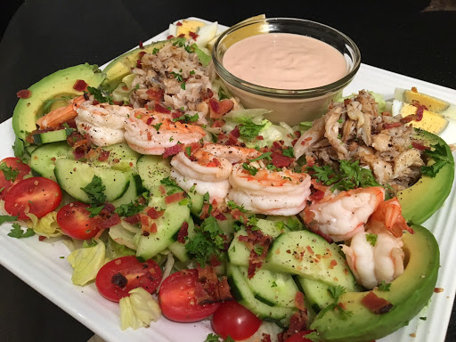 A plate with vegetables, prawns along with a sauce in a glass bowl.