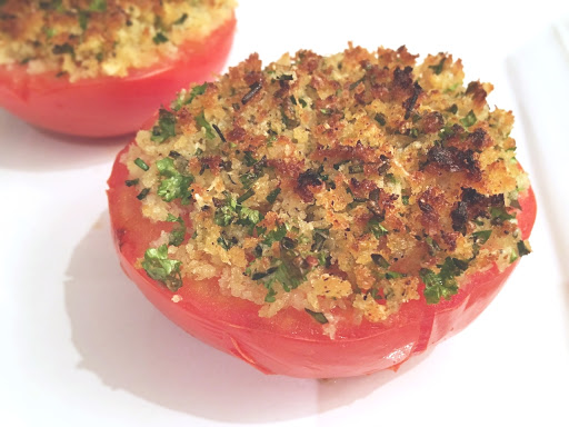 Two halved tomatoes with stuffing on top sitting on a white plate.