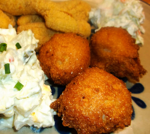 3 hush puppies on plate with potato salad, fried fish and coleslaw.