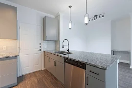 Modern apartment kitchen with stainless steel appliances, granite countertops, and pendant lighting.