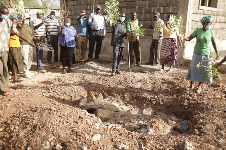 Family members hold twigs pointing at the empty grave of the late Paul Kipchabas in Koroto, Baringo North, on Saturday