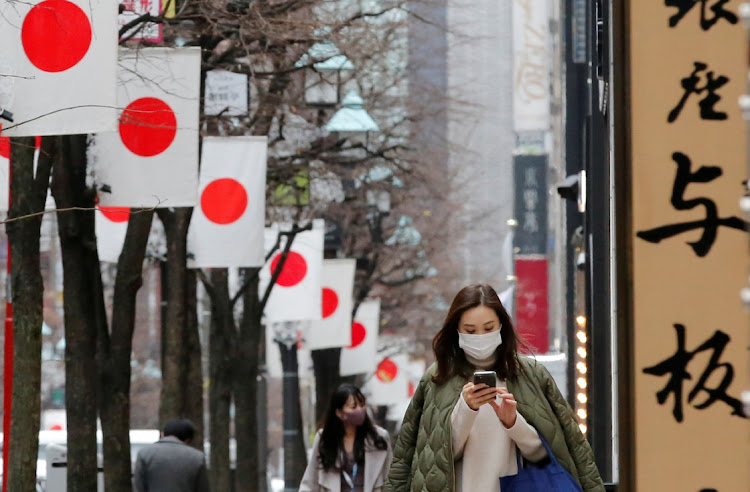 Pedestrians wearing protective masks, following the coronavirus disease (Covid-19) outbreak, walk underneath Japanese national flags at a shopping district in Tokyo, Japan.